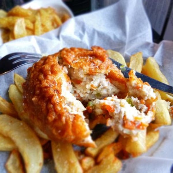 Close-up of a broken fish cake revealing its filling, surrounded by golden french fries.