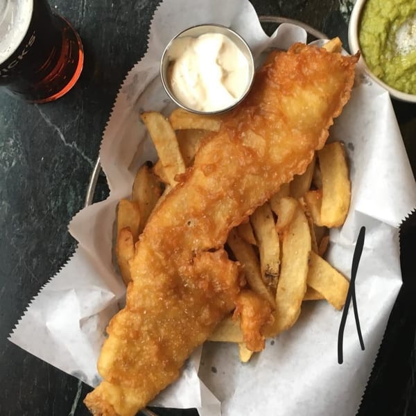 A basket of The Anchor Fish & Chips' golden-brown fish and chips with tartar sauce, mushy peas, and a beer.