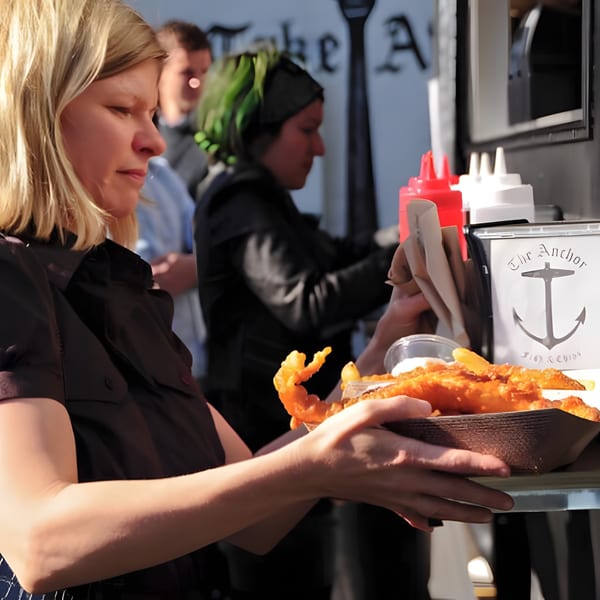 A woman holds a tray of golden-brown fish and chips from The Anchor Fish & Chips.