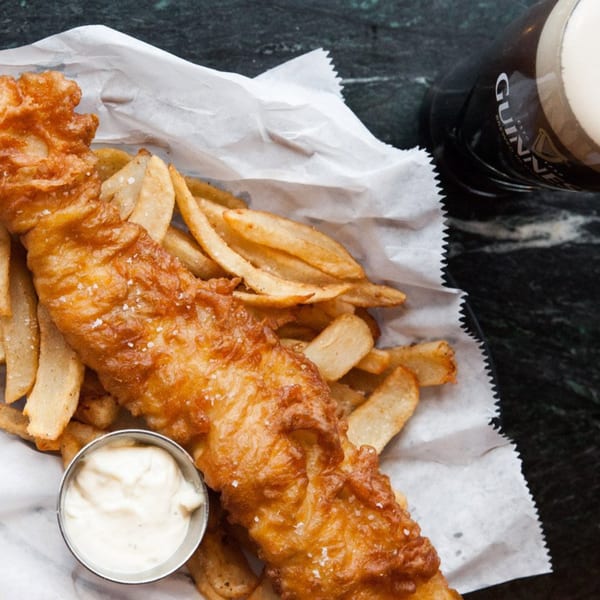 Crispy fish and chips with tartar sauce in a paper-lined basket, next to a pint of Guinness.