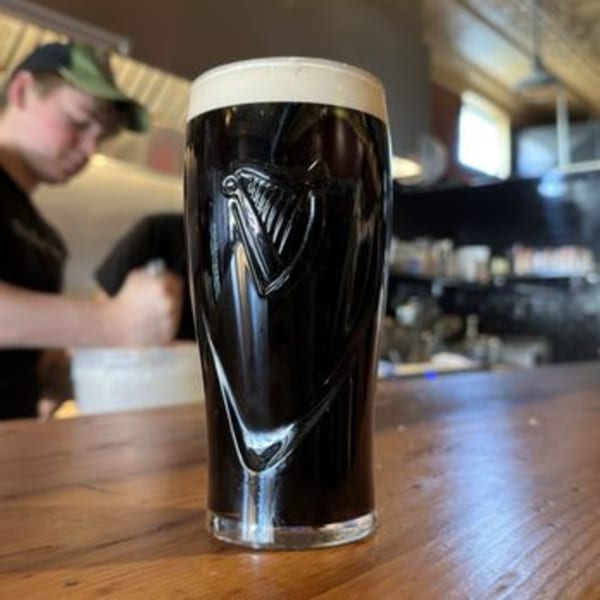 A pint of Guinness beer with a creamy head on a wooden table, with a blurred person in the background.