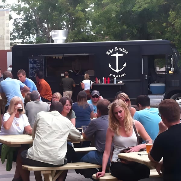 Patrons enjoying food and drinks at outdoor picnic tables in front of The Anchor Fish & Chips food truck.