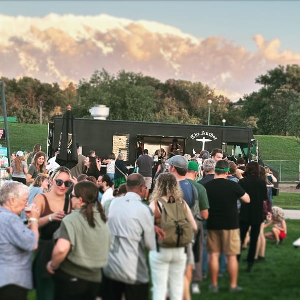 A crowd of people gathered around The Anchor Fish & Chips food truck on a grassy field.
