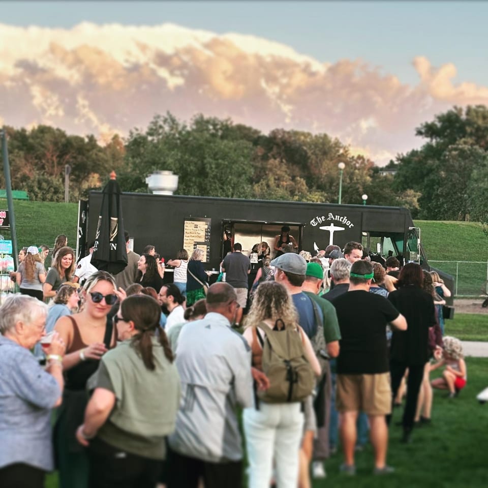 A crowd of people gathered around The Anchor Fish & Chips food truck on a grassy field.